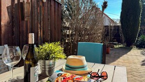 Une table avec une bouteille de vin, une plante en pot, un magazine sur les pizzas, un chapeau de paille et des lunettes de soleil.
