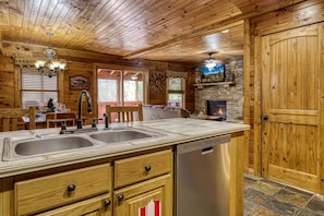 Interior d'una cabana de fusta amb cuina, que inclou un doble rentaplat, armaris de fusta i una llar de pedra.