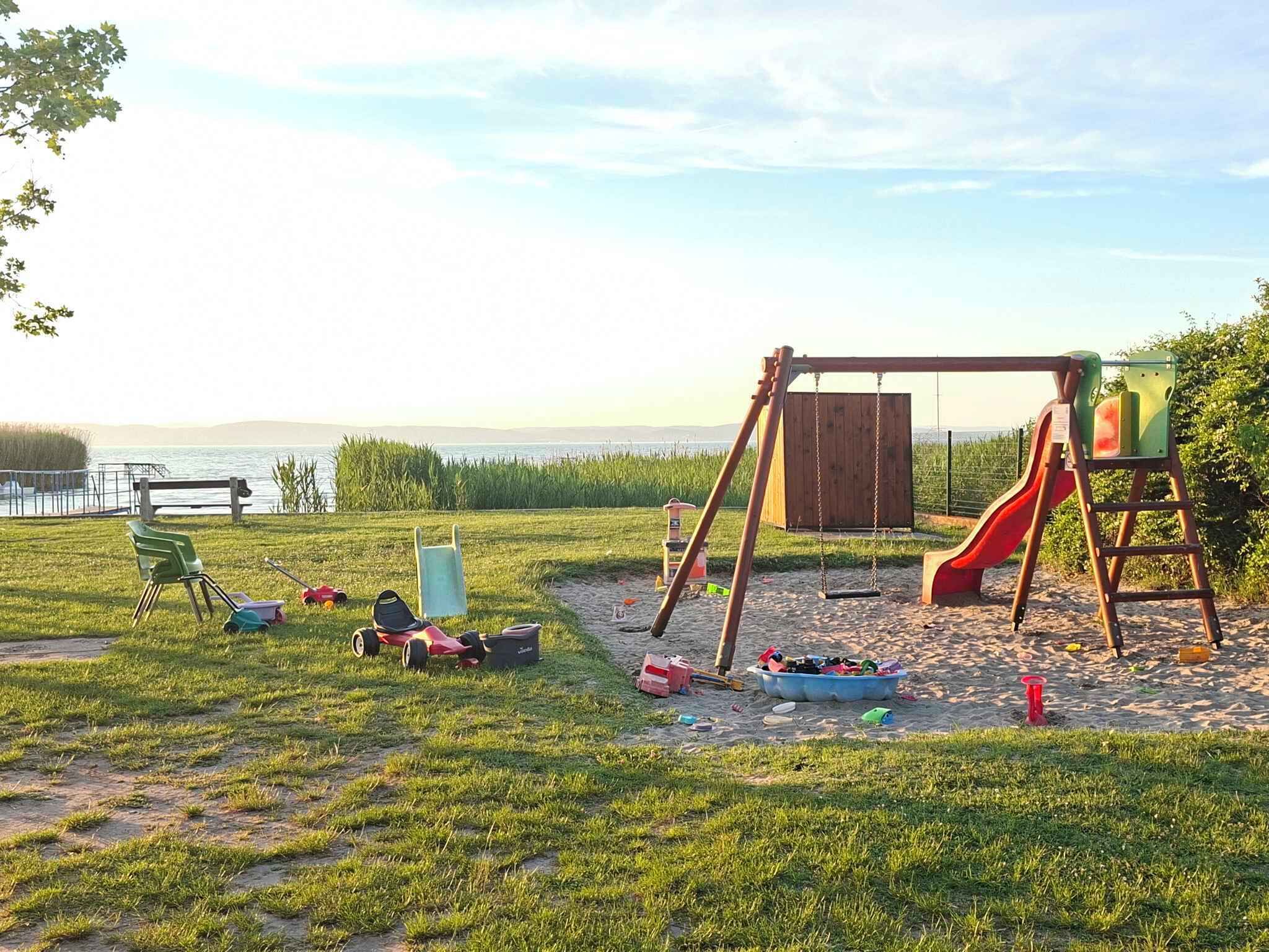 A playground with a swing set and slide, surrounded by grass and a body of water.