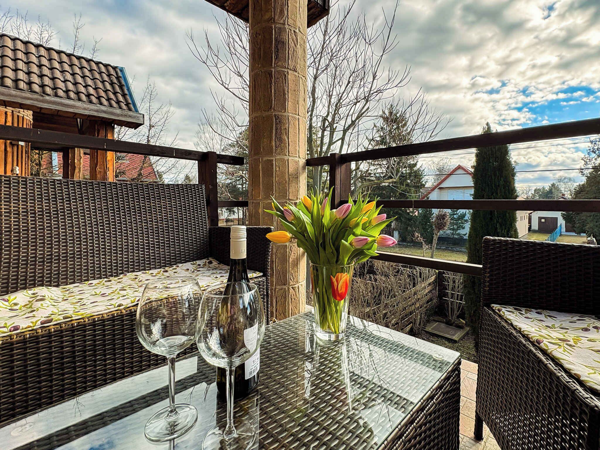 An outdoor seating area with wicker furniture, a glass table, and a bottle of wine.