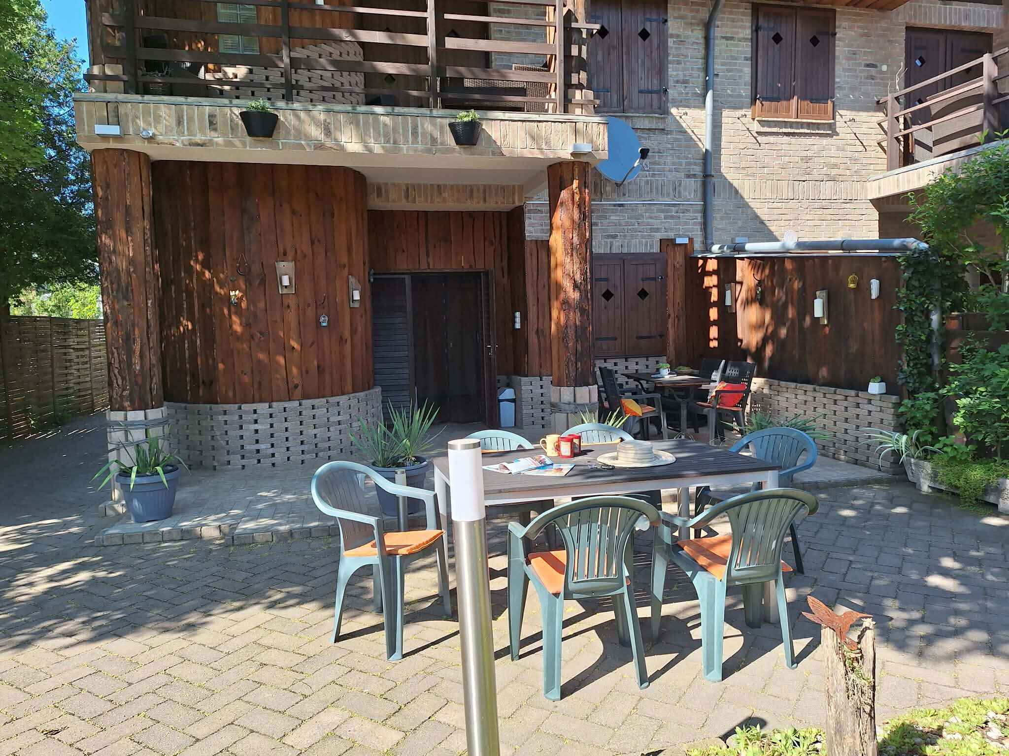 A rustic wooden building with a balcony, outdoor seating area, and a brick wall.