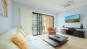 Un soggiorno moderno con un divano bianco, un tavolino da caffè, una TV e una porta scorrevole in vetro che dà su un balcone.
