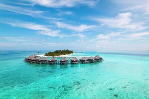 Een overwaterresort met meerdere bungalowachtige accommodaties, verbonden door looppaden, omringd door turquoise water en een klein eiland met begroeiing.