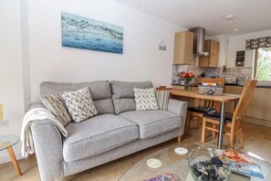 Una sala de estar moderna con un sofá gris, una mesa de centro de vidrio y un cuadro de una escena costera.