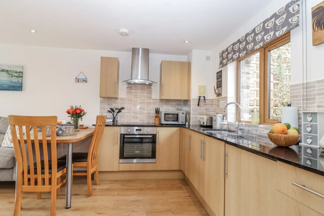 A modern kitchen with wooden cabinets, a stainless steel range hood, a built-in oven, and a large window providing natural light.