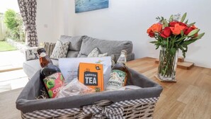 En stue med en grå sofa, en fletkurv med en flaske øl, te og en vase med røde blomster.