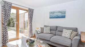 En stue med en grå sofa, et glasbord og et maleri af et kystlandskab.