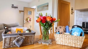A living room with a wooden table, a wicker basket, a vase with flowers, a dog bed, and a couch. - Cawsand Cottage in Cornwall (Saltash)