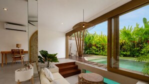 A modern interior with a large window, a pool, and a staircase leading to a balcony. - Sunset Bamboo by Pertama Stay (Kerobokan)