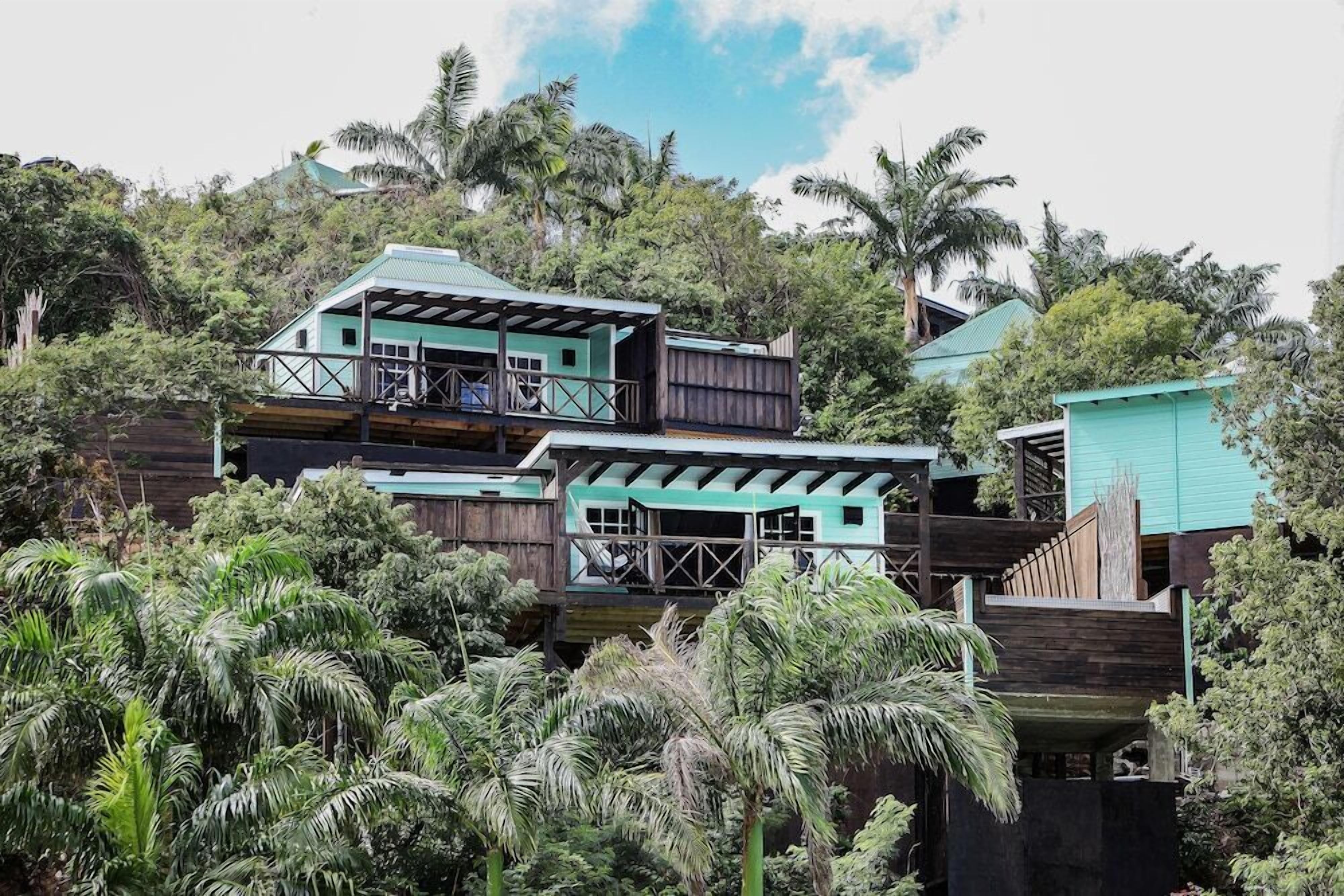 A multi-story wooden house with balconies, surrounded by dense tropical vegetation.