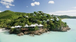 Ein Küstenresort mit mehreren bungalowsartigen Unterkünften, die auf einem üppigen Hügel thronen und einen klaren, türkisblauen Ozean überblicken.