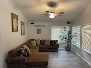A living room with a sectional sofa, a ceiling fan, and a potted plant.