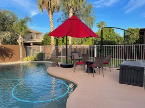 Ein Poolbereich mit rotem Sonnenschirm, Gartenmöbeln und einer umzäunten Terrasse.