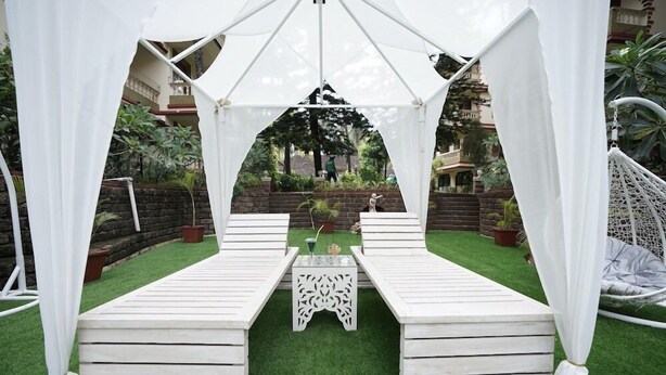 A white tent structure with a table and two benches in a garden area. - Lillywoods Highland Beach Resort (Candolim)