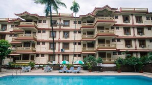 A multi-story hotel with a swimming pool, outdoor seating, and a tropical garden. - Lillywoods Highland Beach Resort (Candolim)