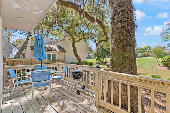 A wooden deck with outdoor furniture, a barbecue grill, and a view of a golf course.