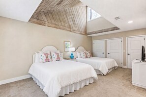 A bedroom with two beds, a desk, a lamp, and a ceiling fan.