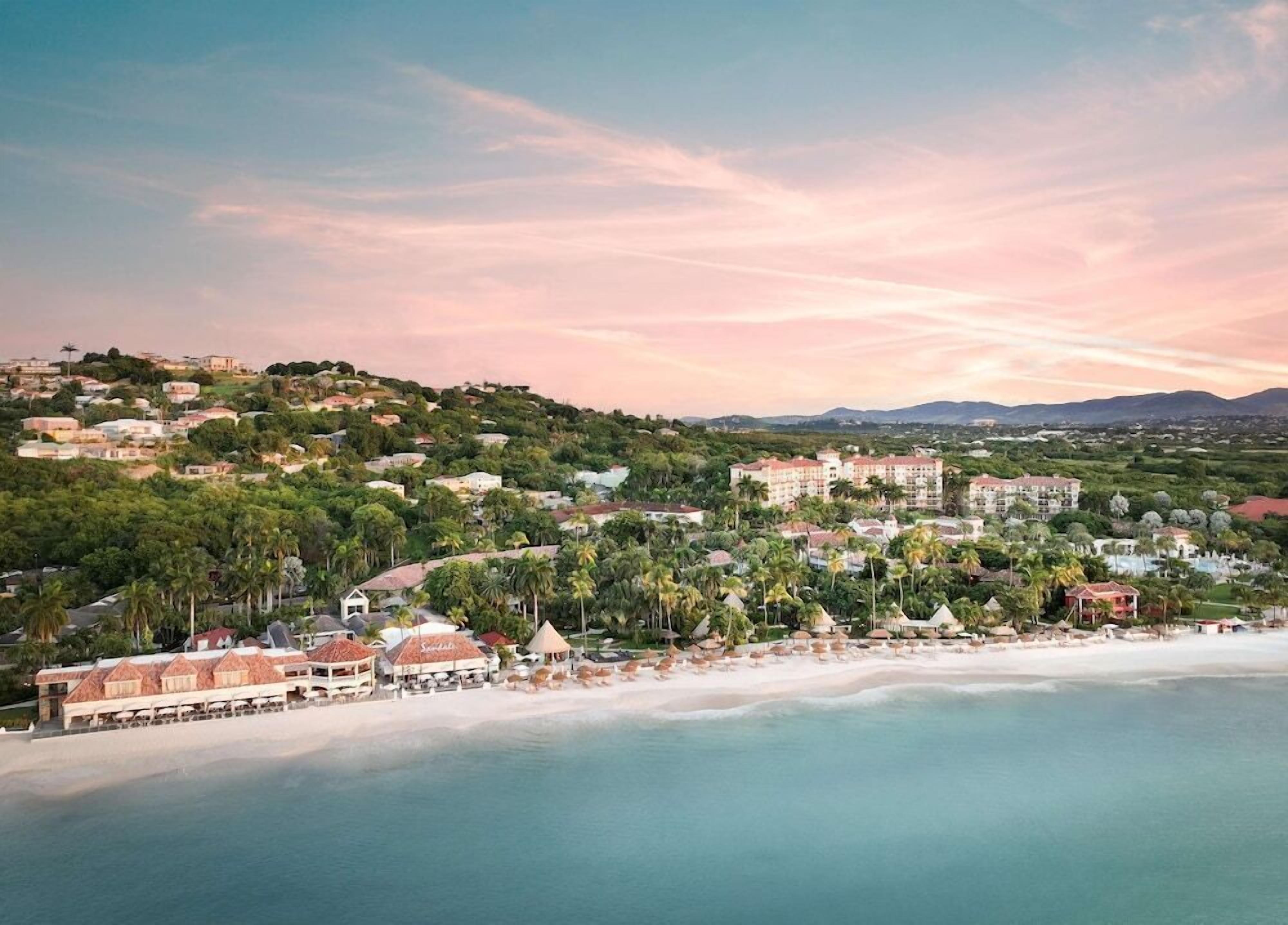 A coastal resort with beachfront villas, a central building with multiple floors, and a beach with umbrellas.