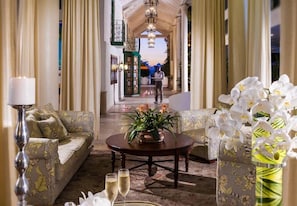 A hotel lobby with a sofa, a table with a vase of flowers, and a view of the outdoor area. - Sandals Grande Antigua (St. John's)