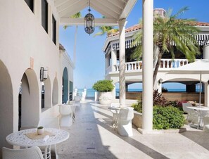 A covered outdoor area with white furniture, palm trees, and a view of the sea. - Sandals Grande Antigua (St. John's)
