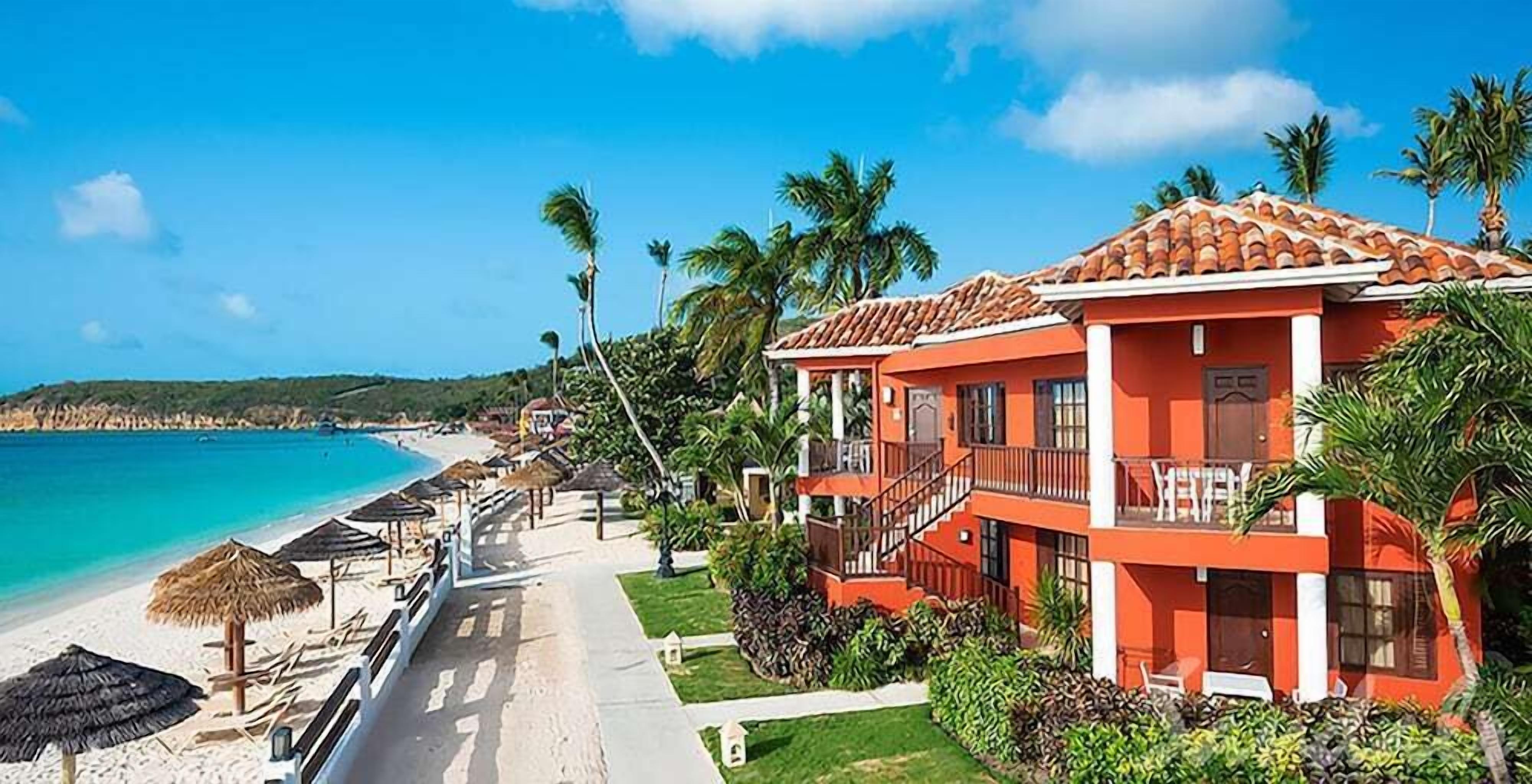 A beachfront hotel with a red facade, balconies, and a clear view of the ocean.