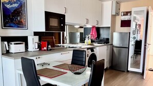 Ett modernt kök med vita skåp, ett matbord med svarta stolar, en mikrovågsugn, ett kylskåp och en tavla på väggen.