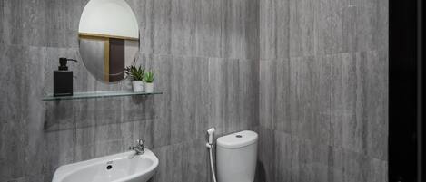 A modern bathroom with a white sink, a toilet, a round mirror, and a glass shelf with a small plant.