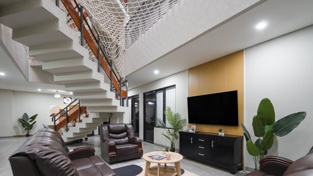 A modern living room with leather sofas, a wooden coffee table, a TV, and a staircase with a netted ceiling.
