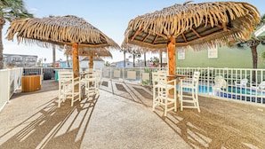 Uma área de estar coberta ao ar livre com guarda-sóis de palha, piscina e vista para o oceano.