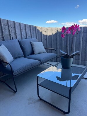 A balcony with a grey sofa and a glass coffee table with a potted orchid. - Blue Moon Apartment-Epic Mountain views Wanaka. (Wānaka)