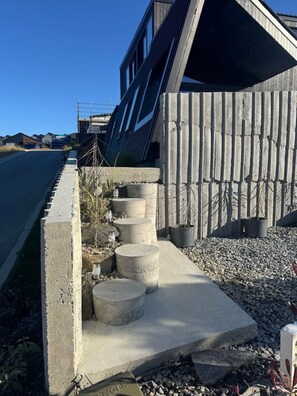 A modern building with a sloped roof and a concrete pathway leading to a wooden fence. - Blue Moon Apartment-Epic Mountain views Wanaka. (Wānaka)