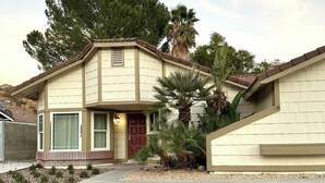 Una casa de dos pisos con fachada color beige, una puerta principal roja y un pequeño porche.