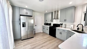 Una cocina moderna con armarios grises, un refrigerador de acero inoxidable, una estufa negra y una encimera blanca.