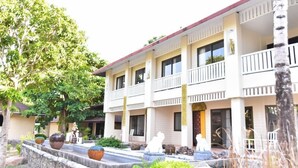 A multi-story hotel with a white facade, balconies, and a landscaped courtyard with planters and sculptures. - Koh Hai Fantasy Resort and Spa (Ko Lanta)
