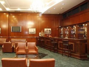 Eine Lobby mit Ledersitzmöbeln, einem Barbereich mit einer Glastheke und gerahmten Bildern an den Wänden.