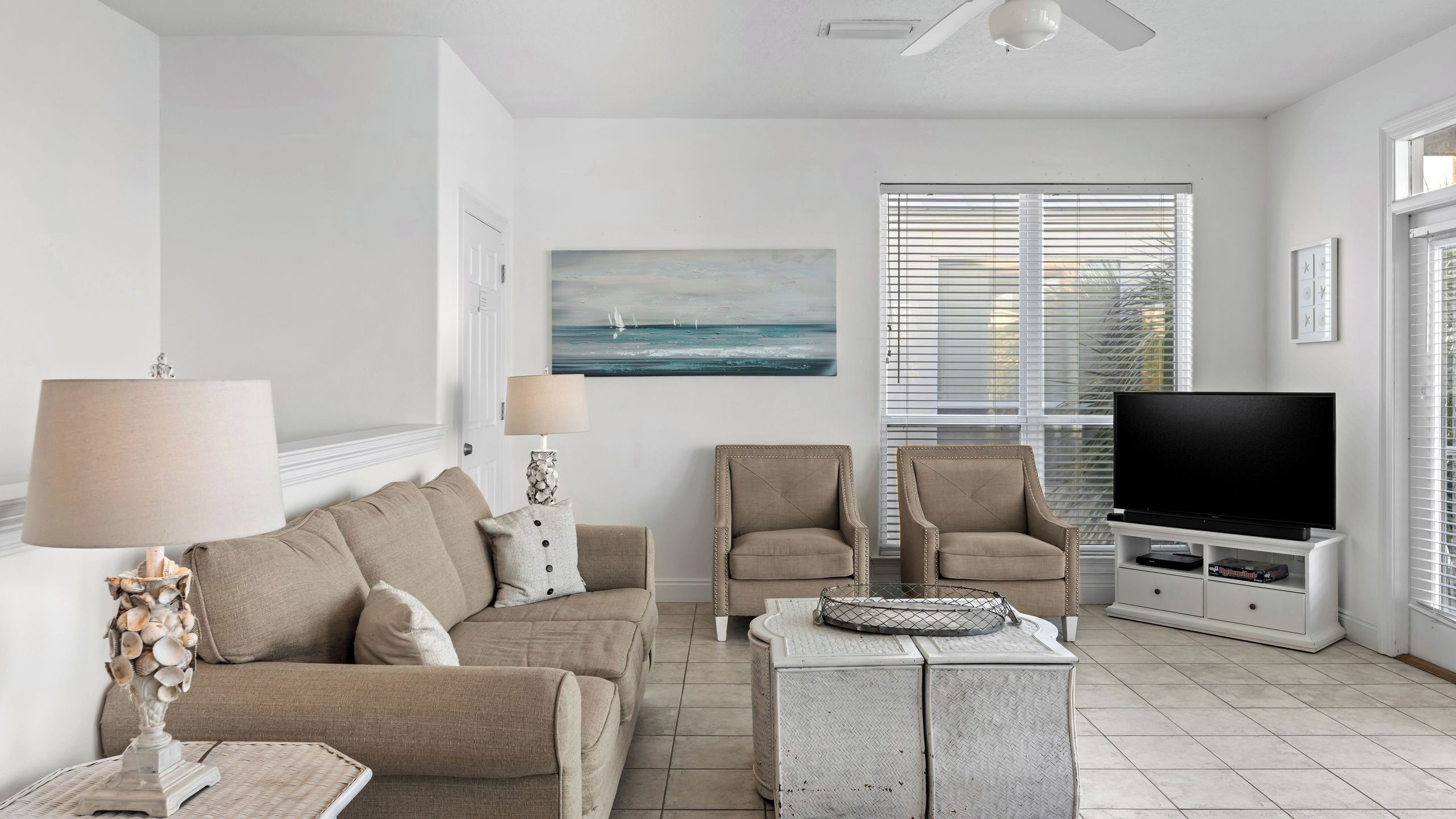 A living room with a sofa, two armchairs, a coffee table, a TV, and a painting of a seascape.