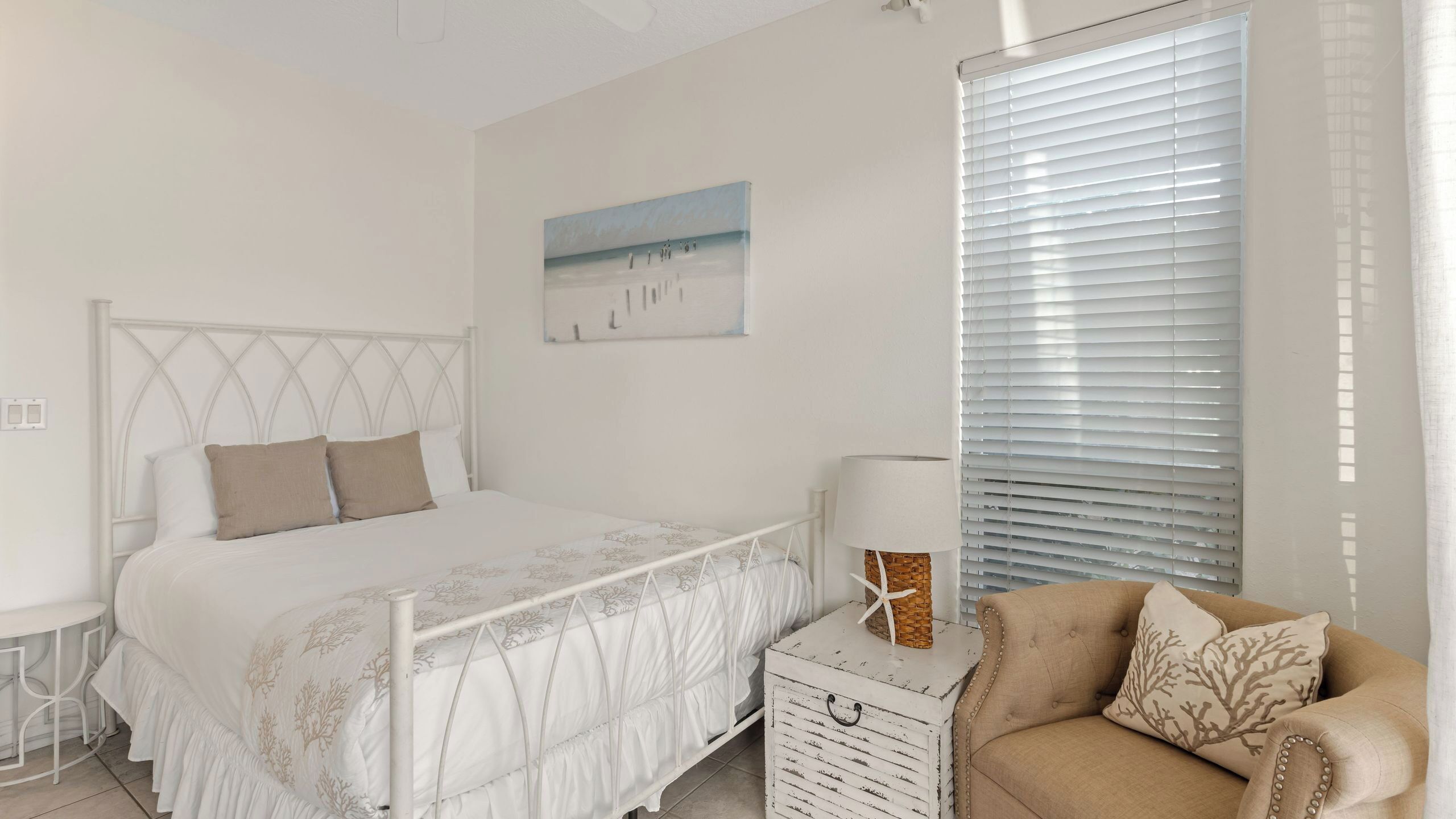 Un dormitorio con cama, mesita de noche con lámpara, una silla y ventana con persianas.