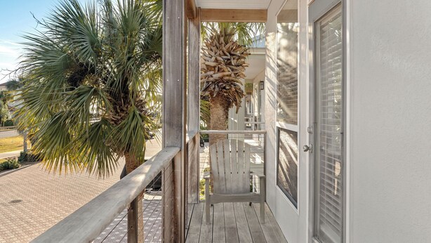 Un balcón de madera con una palmera, un banco de madera y una puerta blanca.