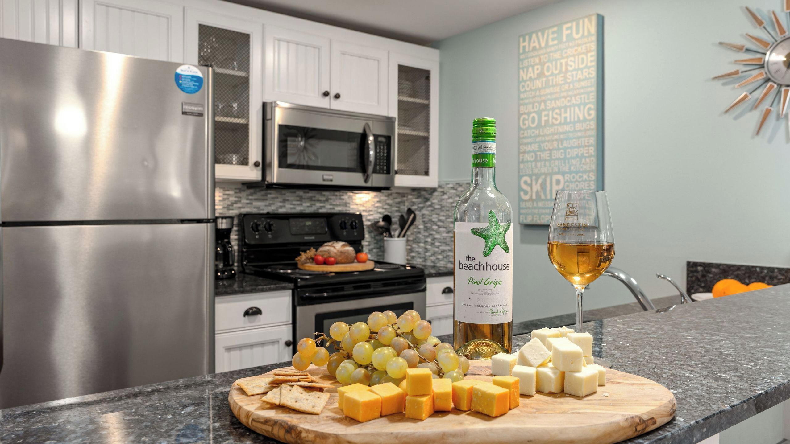 Une cuisine équipée d’appareils électroménagers en acier inoxydable, une planche à découper en bois avec du fromage et des raisins, une bouteille de vin et un verre de vin.
