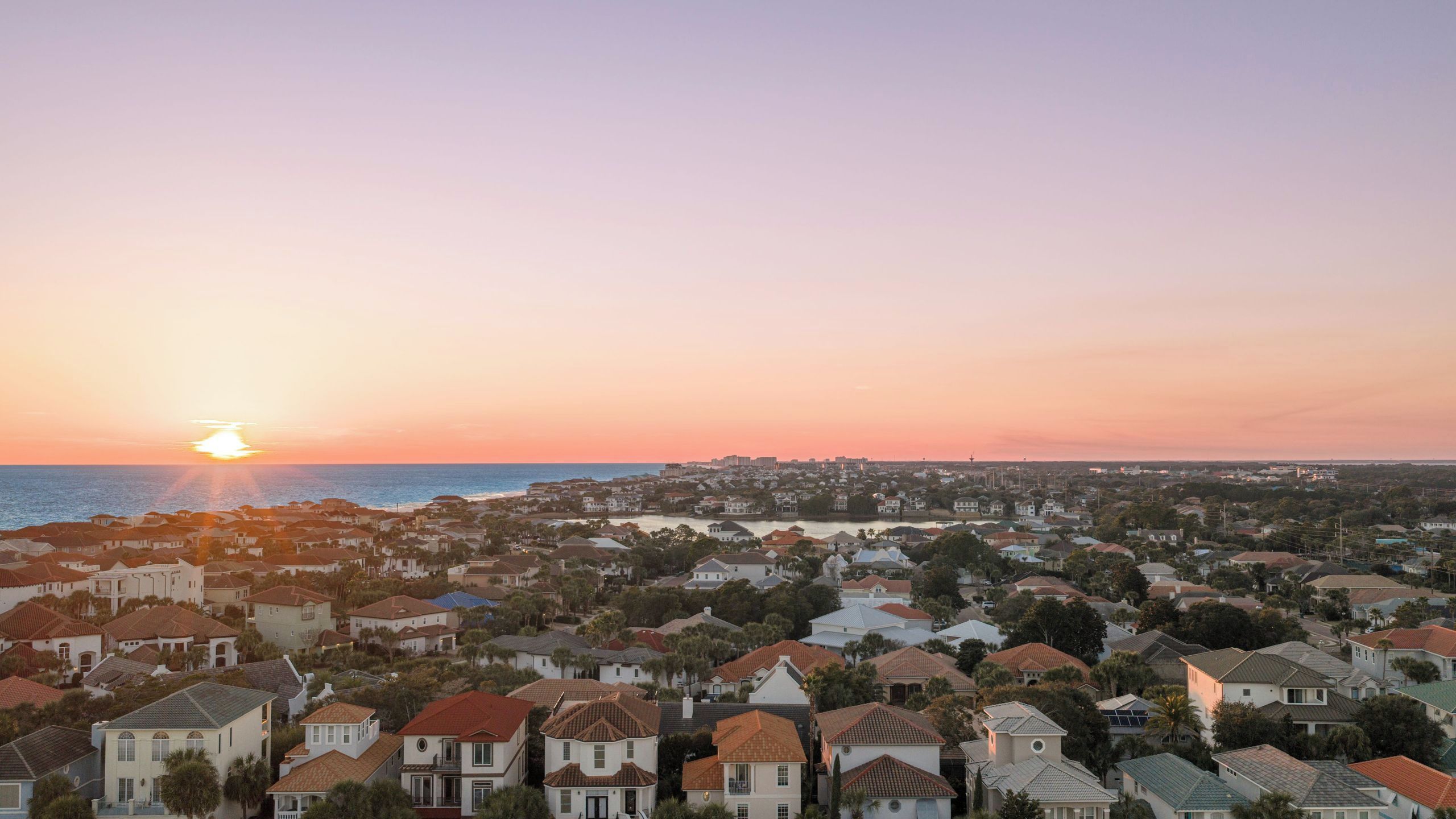 Et kystnære boligområde med huse, klar himmel og solnedgang over havet.