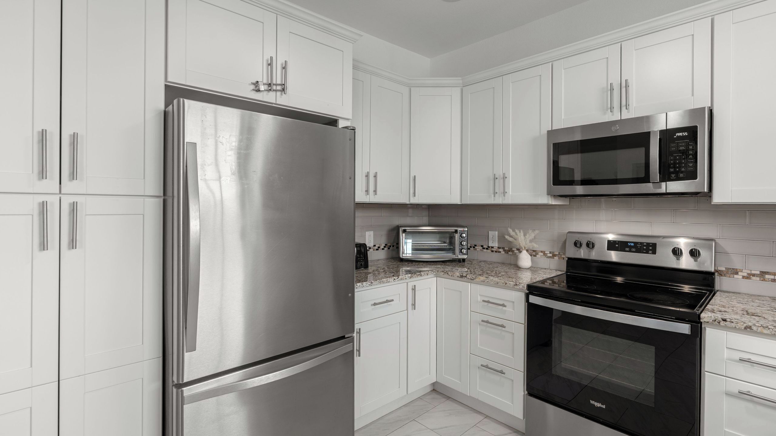 A modern kitchen with stainless steel appliances, white cabinetry, and a tiled backsplash.