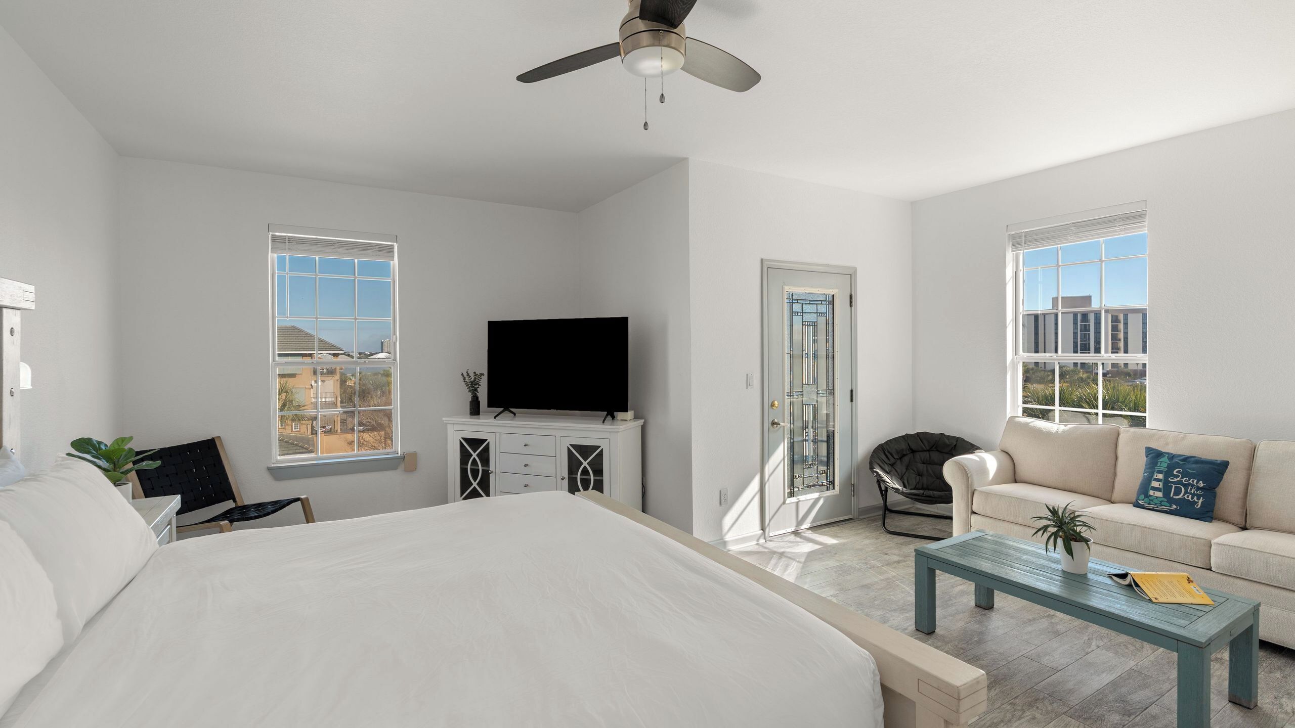 A bedroom with a bed, a TV, a ceiling fan, and a view of the outside.