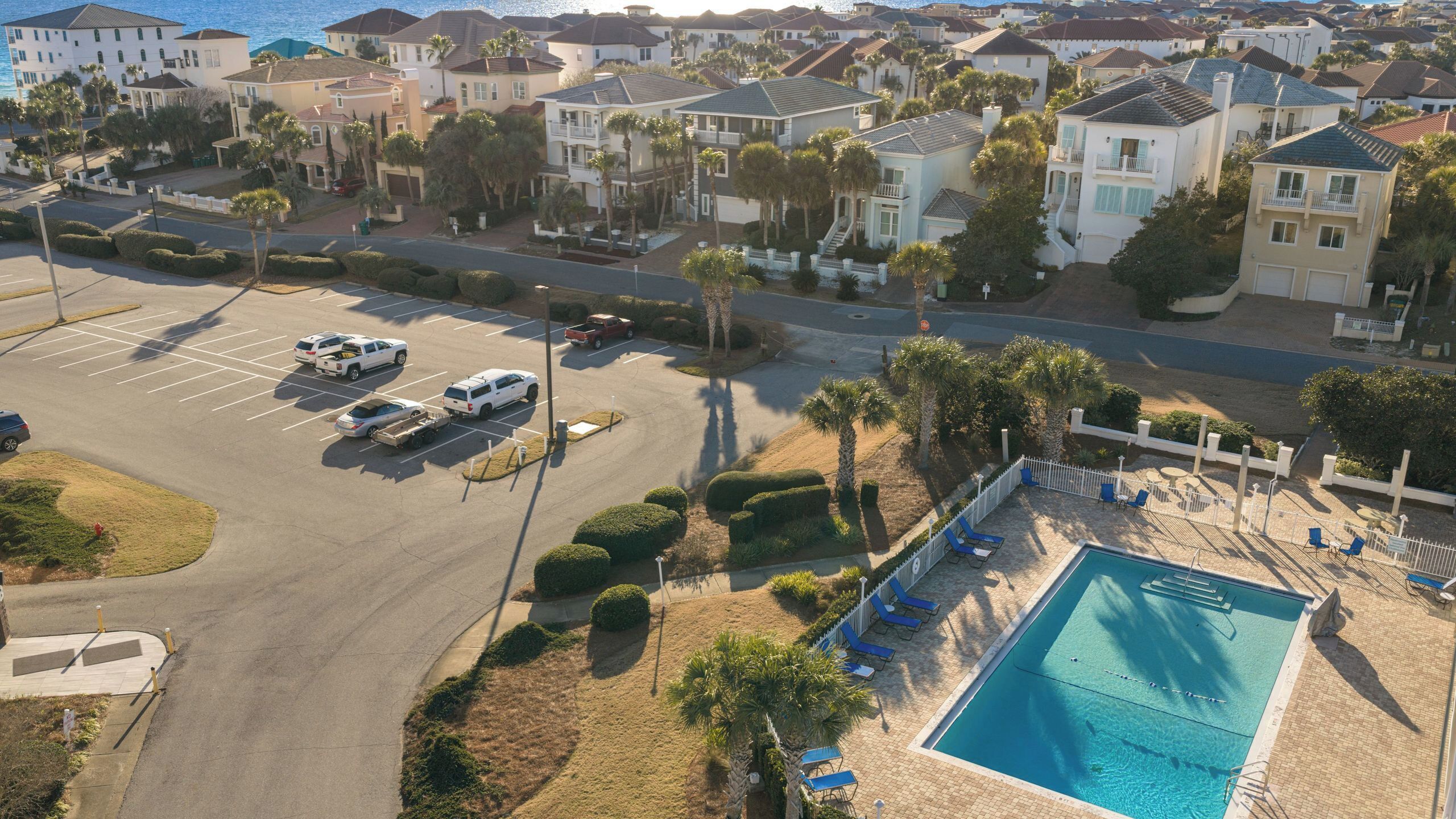 A residential area with a swimming pool, parked vehicles, and houses with balconies.