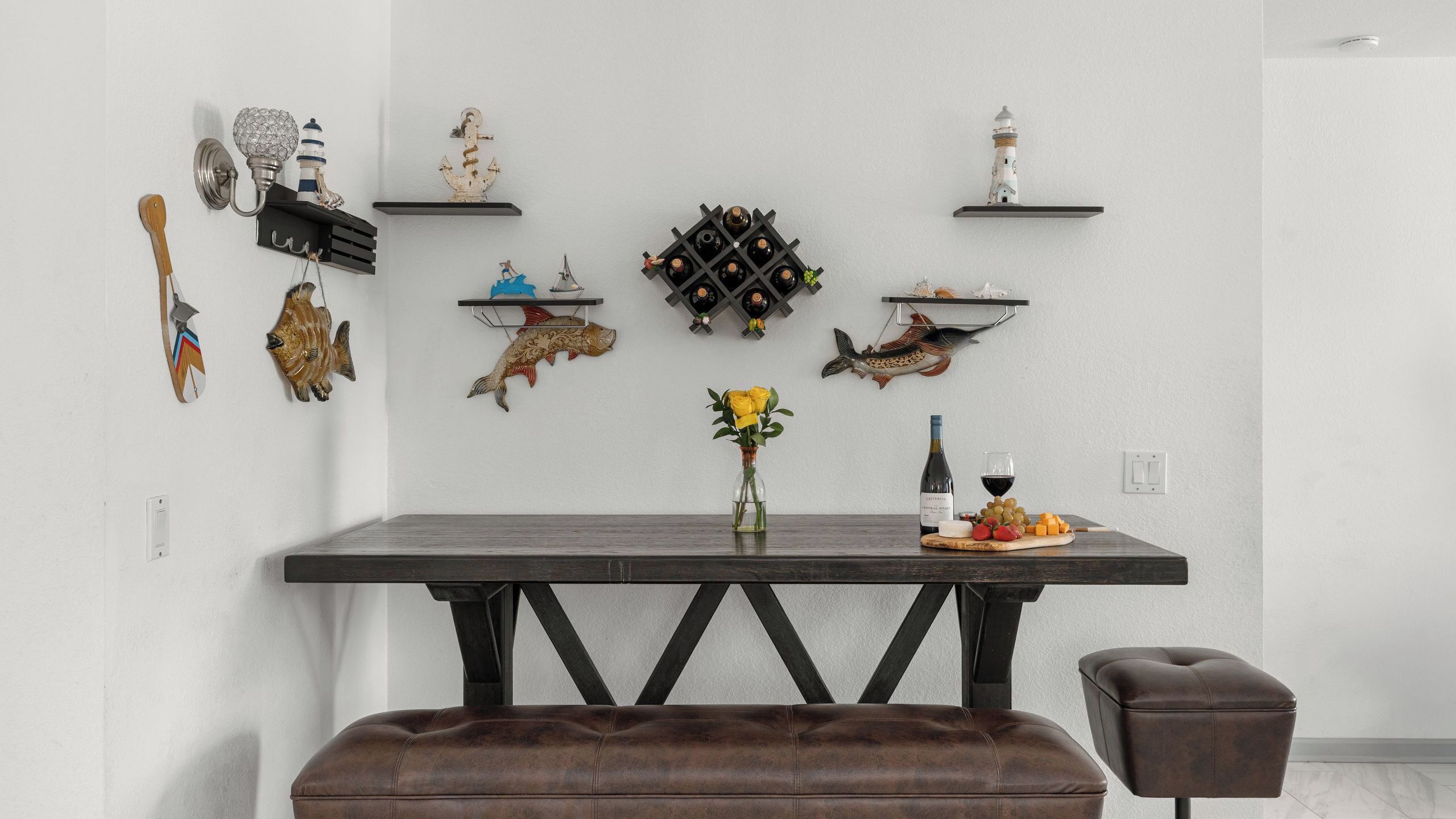 A dining area with a dark wooden table, a bench, and various wall decorations including lighthouses and fish.