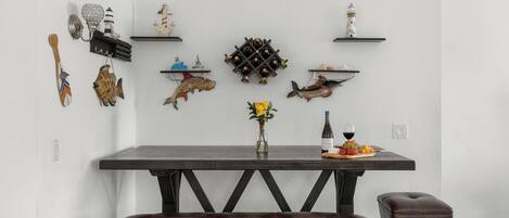 A dining area with a dark wooden table, a bench, and various wall decorations including lighthouses and fish.