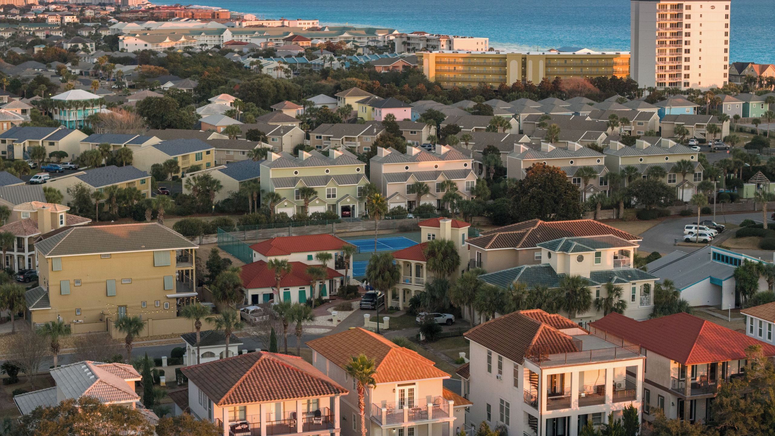 Un quartier résidentiel situé sur la côte, avec une variété de maisons, dont certaines ont des toits rouges, et un grand immeuble avec des balcons en arrière-plan.