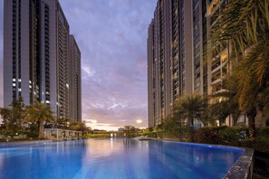Una piscina rodeada de edificios residenciales altos, con un atardecer de fondo.