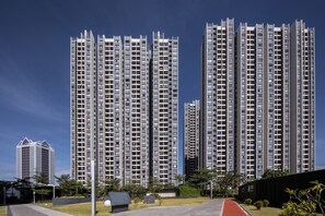 Um edifício residencial alto com várias varandas, área ajardinada com árvores e céu claro.