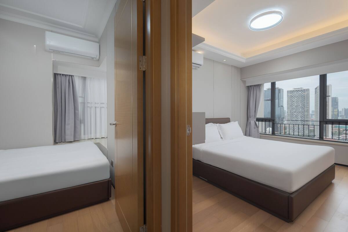 A hotel room with two beds, a large window with a city view, and an air conditioning unit.