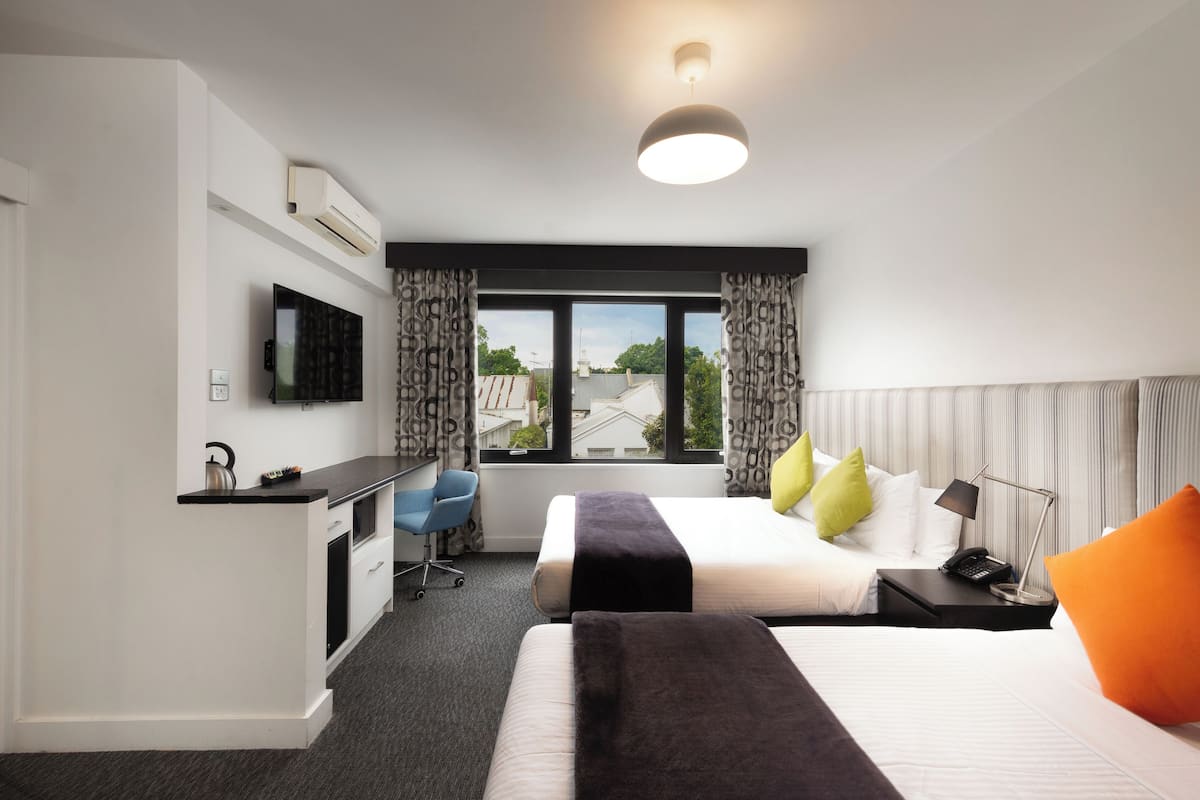 Habitación de hotel con cama, mesita de noche, lámpara y escritorio con silla.